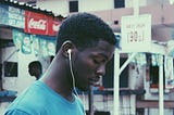 A young man in an urban background quietly looks at the ground while walking