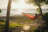 Person in silhouette sitting in a red hammock overlooking the ocean