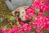 Woman laying down on the grass by some pink flowers
