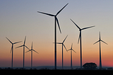 A rad view of wind turbines against a sunset