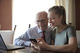 A young woman showing an elderly gentleman how to use a smartphone