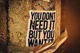 A photo of a poster stuck on to a wall with the words ‘you don’t need it but you want it’ on it