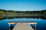 A dock extending into a calm lake against a blue sky