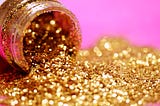 gold glitter spilling out of an open container. the background of the picture is bright, girly pink.