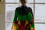 A Child stood in front of a window with a vibrant-colored cloak.