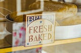 An image of a bakery shelf that has a sign saying fresh bread. Inside there are a couple of breads.