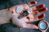 A hand holds a crystal, dried herbs, and a crystal pendulum.