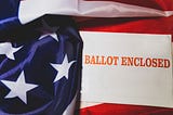 An envelope that says “BALLOT ENCLOSED” in red interlaced with the American flag