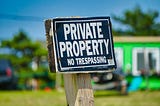Private Property, No Trespassing sign on wooden stake, posted in front of small green house.