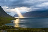 A scenery with the Sun beam pouring through dark clouds on water.