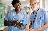 Smiling female nurse showing an electronic health record on a digital tablet to male hospital colleague