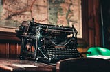 A gorgeous, antique black typewriter with a blank sheet of paper lying next to it, on a wooden desk.