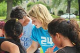 A blonde woman helping some children with an activity.