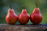 Three reddish pears sitting on a log