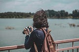 A woman holding a camera on a bridge while looking away at the river