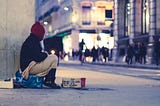 Homeless man sitting on the pavement with few possessions around.