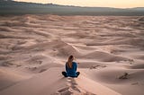 A woman sitting in the sand alone.