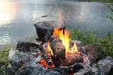 A large cauldron above an open fire, near a water body