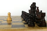 chess board with just one white pawn up against an entire fleet of black chess pieces, lined up.