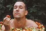 A man holding an apple while bathing in a tub full of apples