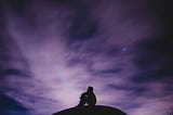 A photo of a man on top of a hill at night by himself, looking out into the universe. It represents the existential questions this poem asks.