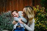 A woman with a young child. She is tickling him, he is laughing a lot and she is smiling.