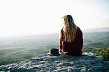 A girl sitting on a cliff looking out into the distance.