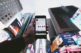 Hand holding phone featuring Instagram profile in front of Times Square in New York City.