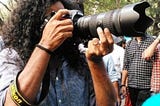 Young man in a crowd with long curly hair holding a Nikon camera with zoom lens