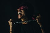 A blindfolded man trying hard to break free from a chain