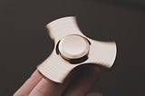 a metallic fidget spinner in motion on someone’s fingertips