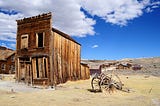 View of old Wild West ghost town with a dilapidated wooden storefront and an abandoned cart in the foreground.
