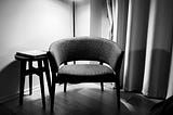 Black and white photo of an empty chair in the corner of a room