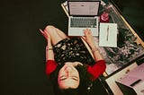 A young woman, the author, sits at a desk with a laptop and smiles.