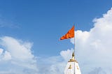 A saffron flag flying proudly on top of a Hindu temple with blue skies behind