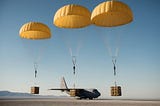 A group of cargo parachutes descending from a military transport aircraft, releasing supplies over a remote area