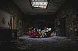 A dark abandoned room, strewn with garbage with graffiti on the walls. In the middle of the room sits a variety of toys that will never make it to the store shelves.