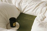 An olive green book of Shakespeare nestled in a white duvet with a cup and saucer