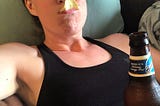 A woman laying on a couch with a chip in her mouth, holding a beer.