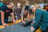 Four Makers students standing around a laptop talking and smiling
