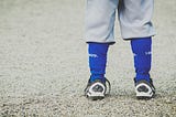 The feet of a small child in a baseball uniform.