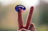 Two fingers in the air with an “I Voted” sticker on the left finger
