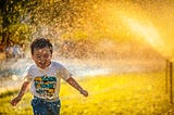 child playing in sprinkler