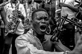 A musician yells out while performing, surrounded by members of a band