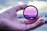 A UV-like lens being held by a left hand’s thumb and forefinger.