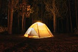 A glowing yellow camp tent in a forest at night