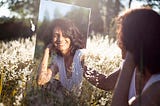 woman in field looking in mirror- New Chapter, New Me: Crafting Your Narrative After Fifty