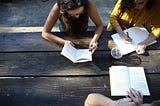 Three people sit around a table, reading.