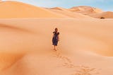 Woman in a black dress walking through a desert.