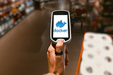 A shopper pushing a cart and holding a bar-code scanner with the docker logo on it.